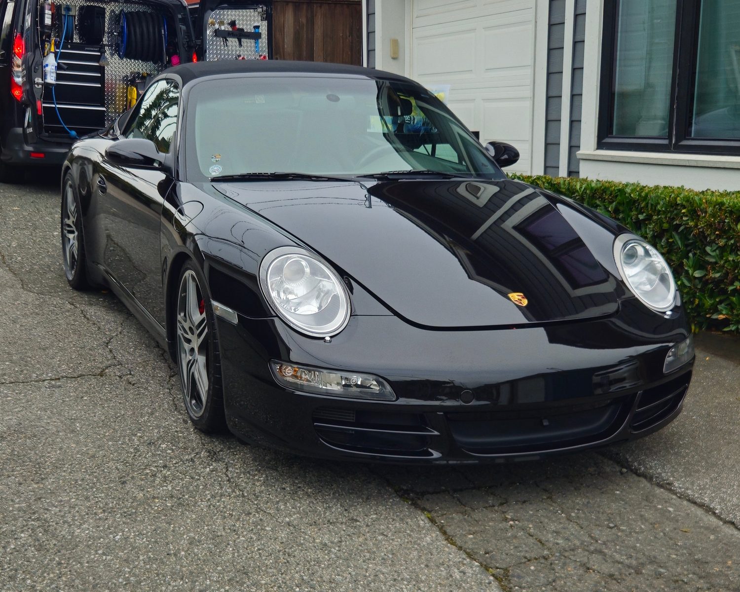 Glossy black Porsche 911 after detailing, with the Vantique Detailing mobile van behind it